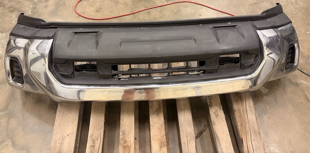 Chrome front bumper assembly with black upper trim and grille opening, on a pallet