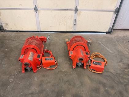 Two orange pipe grooving machines side by side on a concrete floor, each with its own foot switch and cord