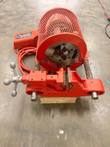 Grooving machine from the clamp side: open V-jaw vise, round mesh motor guard and chuck head, on a wood block