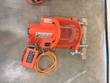 Orange Aeroquip grooving machine from above on the floor, clamp rods resting on a wood block, foot switch and cord