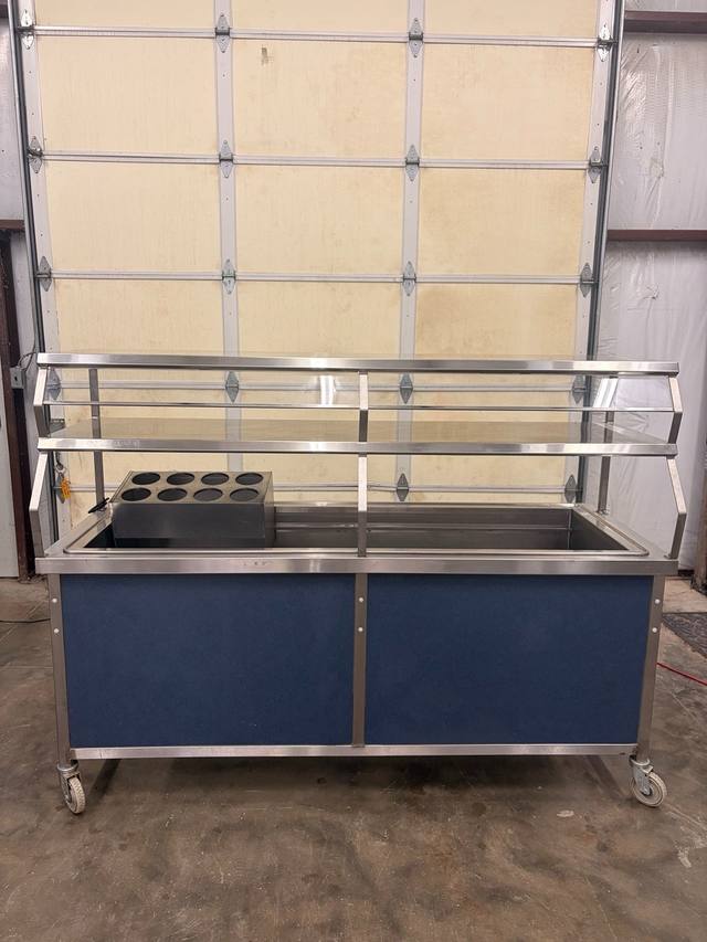 Stainless steel serving cart with blue front panels, glass sneeze guard, two-tier shelf and eight-hole utensil holder