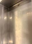 Inside corner of the stainless pan with a round drain strainer near the top and a vertical trim strip