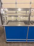 Left half of the front of the Atlas Metal cold food counter with blue laminate panels and stainless sneeze guard