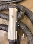 Handheld induction transformer with aluminum body, brass clamp and lifting shackle lying on braided cooling hoses