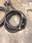 Coiled braided cable with handheld induction transformer on a concrete floor, generator cabinet at the top edge