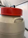 Red insulated lid and steel carry handle on a cream cryogenic dewar, with worn paint and tape on the handle