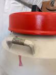 Carry handle wrapped in worn tape beside the red lid on a cream cryogenic dewar