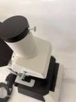 Trinocular camera port with black cap and set screw on the white microscope head, stage below