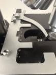 Silver mechanical slide holder with two thumbscrews and measuring scales on the black stage