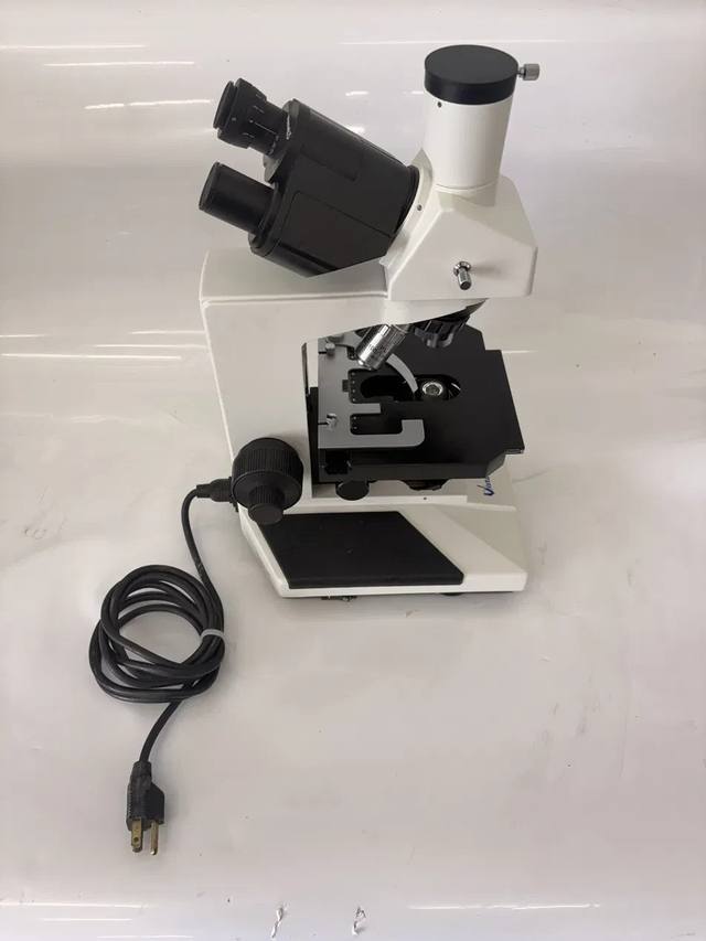 White trinocular microscope with binocular head, mechanical stage and power cord coiled beside the base