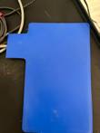 Flat blue pad with a tab and attached cable lying on a black tray