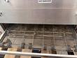 Stainless wire-mesh conveyor belt of the Lincoln Impinger oven with a hot surfaces warning label