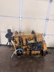 Yellow Caterpillar diesel engine from the side, with cooling fan, blue hose, oil filters and flywheel housing