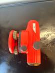 Red automatic level on its side showing the leveling foot screws, horizontal circle and focus knobs