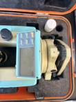 Theodolite laid in its case, keypad and LCD at center, tribrach with leveling screw at right, cropped by the frame