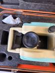 Top view of a teal and cream theodolite telescope lens in its fitted case, silica gel pack beside it