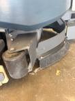 Front corner of the Nilfisk Liberty SC60 showing a black roller wheel and bristle brush with guard
