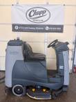 Nilfisk Liberty SC60 ride-on floor scrubber seen from the side in front of a Chupp Surplus banner