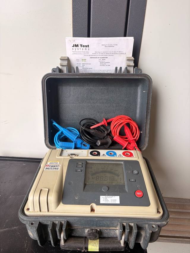Insulation tester in its open case with three test leads and the calibration paper in the lid