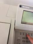 Beckman DU520 screen showing System Checks menu, with a finger pressing a key above the numeric keypad