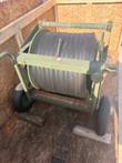 Two-wheel military green hose reel cart with a full spool of black hose in a wooden crate