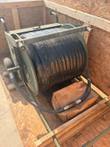 Wheeled hose reel with full black hose spool in a wooden crate, hose end resting on a brown bag