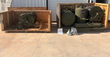 Two open crates: wheeled hose reel at left, green tanks and reel skid at right, with funnel and manual