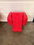 Red carrier stood on its end with the two end doors folded against the body, steel pivot screws visible
