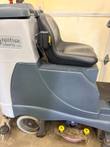 Side of Nilfisk Liberty SC60 scrubber: black seat, dark gray body panel, wheel and yellow-knobbed scrub deck