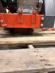 Underside edge of the orange saw frame with engine mounting brackets, bolts and a wheel, on a pallet