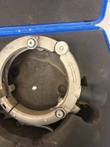 Rotary peeler ring with direction arrow, tension spring and black rubber handle in case foam; left side cropped